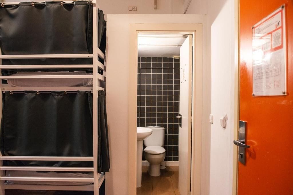 Un pasillo estrecho con una puerta blanca que da a un baño con inodoro y lavamanos.