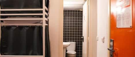 Un pasillo estrecho con una puerta blanca que da a un baño con inodoro y lavamanos.