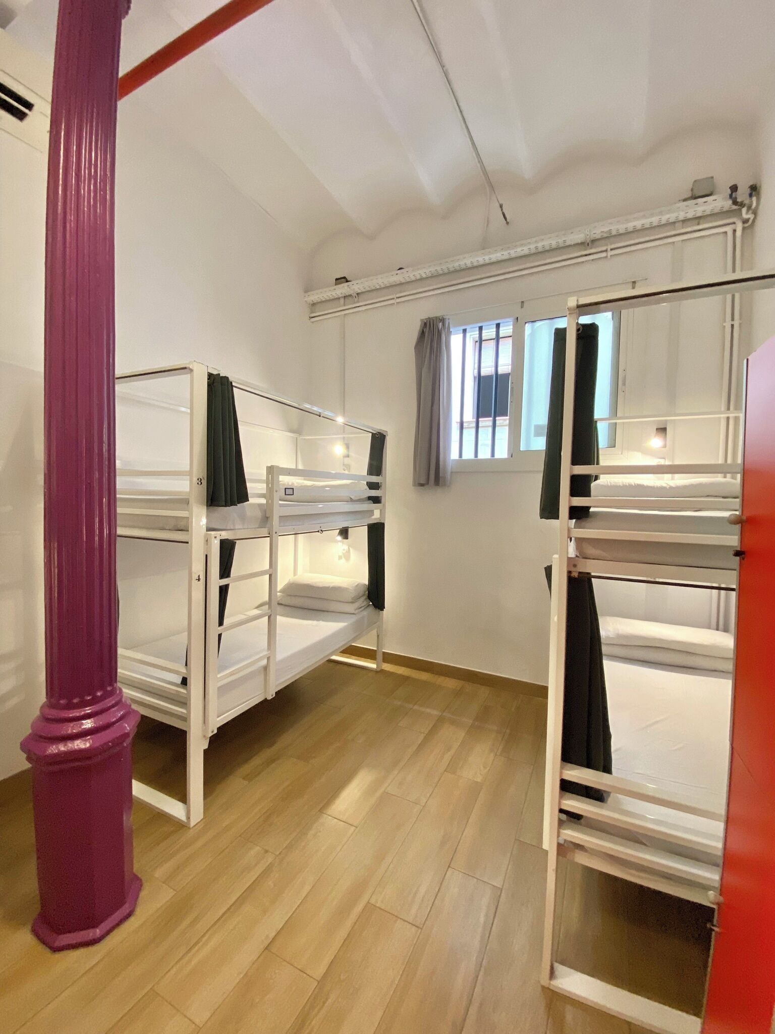 Ein Schlafsaalzimmer mit Etagenbetten, Holzboden, einem Fenster mit Vorhängen und einer weißen Decke.