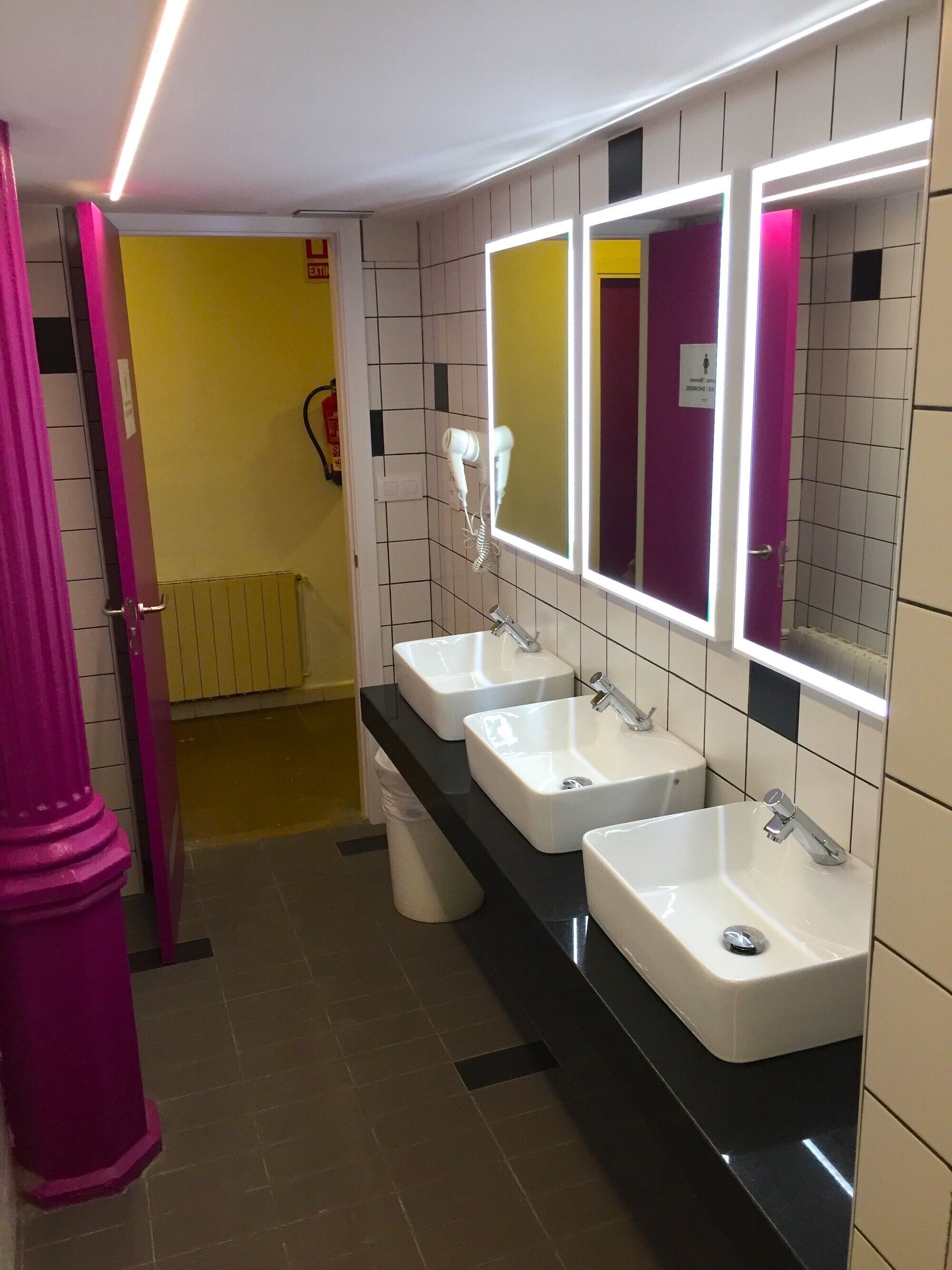 A bathroom with three sinks, a mirror, and a yellow door in the background.