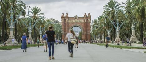 A wide pedestrian pathway lined with palm trees and decorative street lamps, leading to a large, ornate archway.