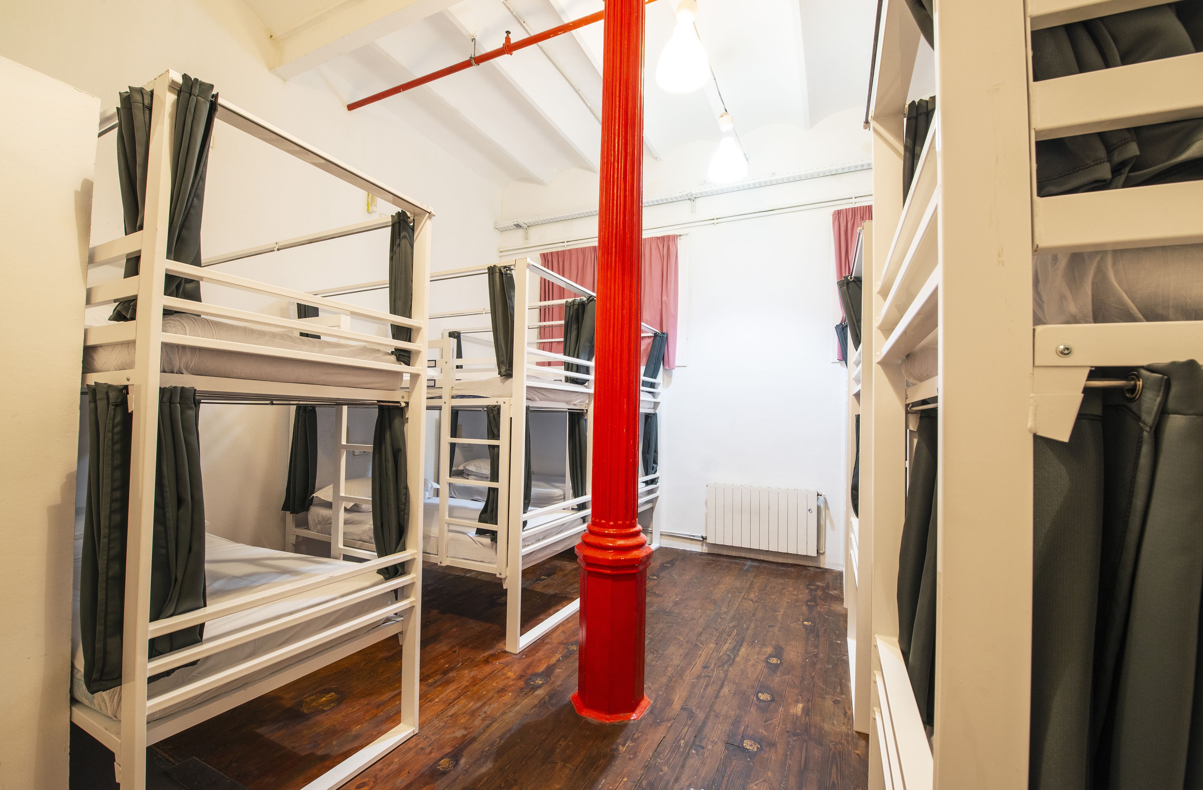 Ein Schlafsaalzimmer mit Etagenbetten, einer roten Säule und Holzboden.