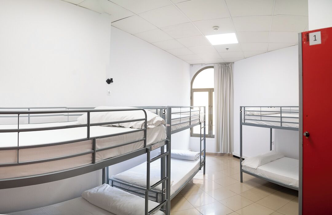 Ein Schlafsaalzimmer mit Etagenbetten, einer roten Tür und einem Fenster mit Vorhängen.