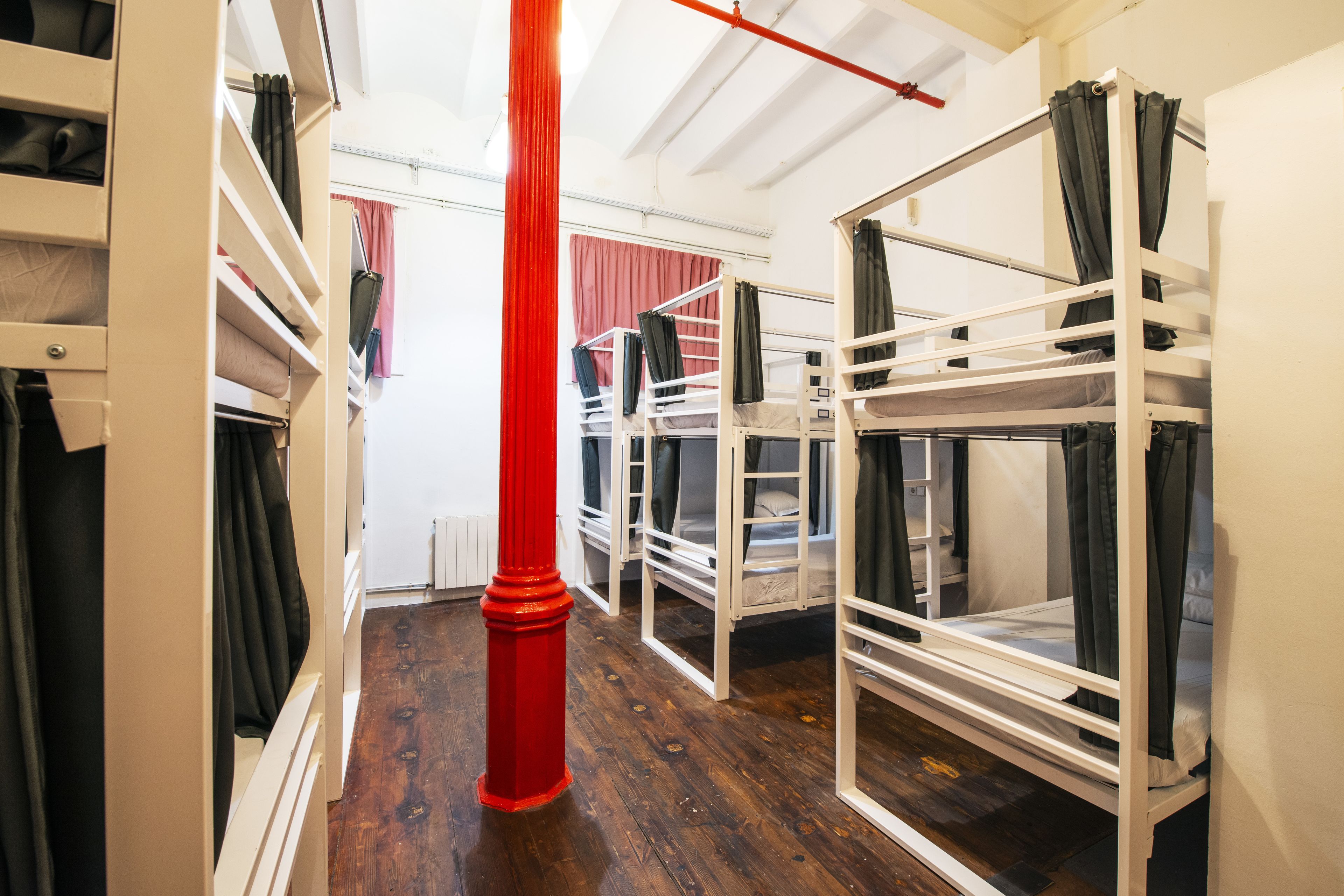 Une chambre de dortoir avec des lits superposés, un pilier rouge et un plancher en bois.