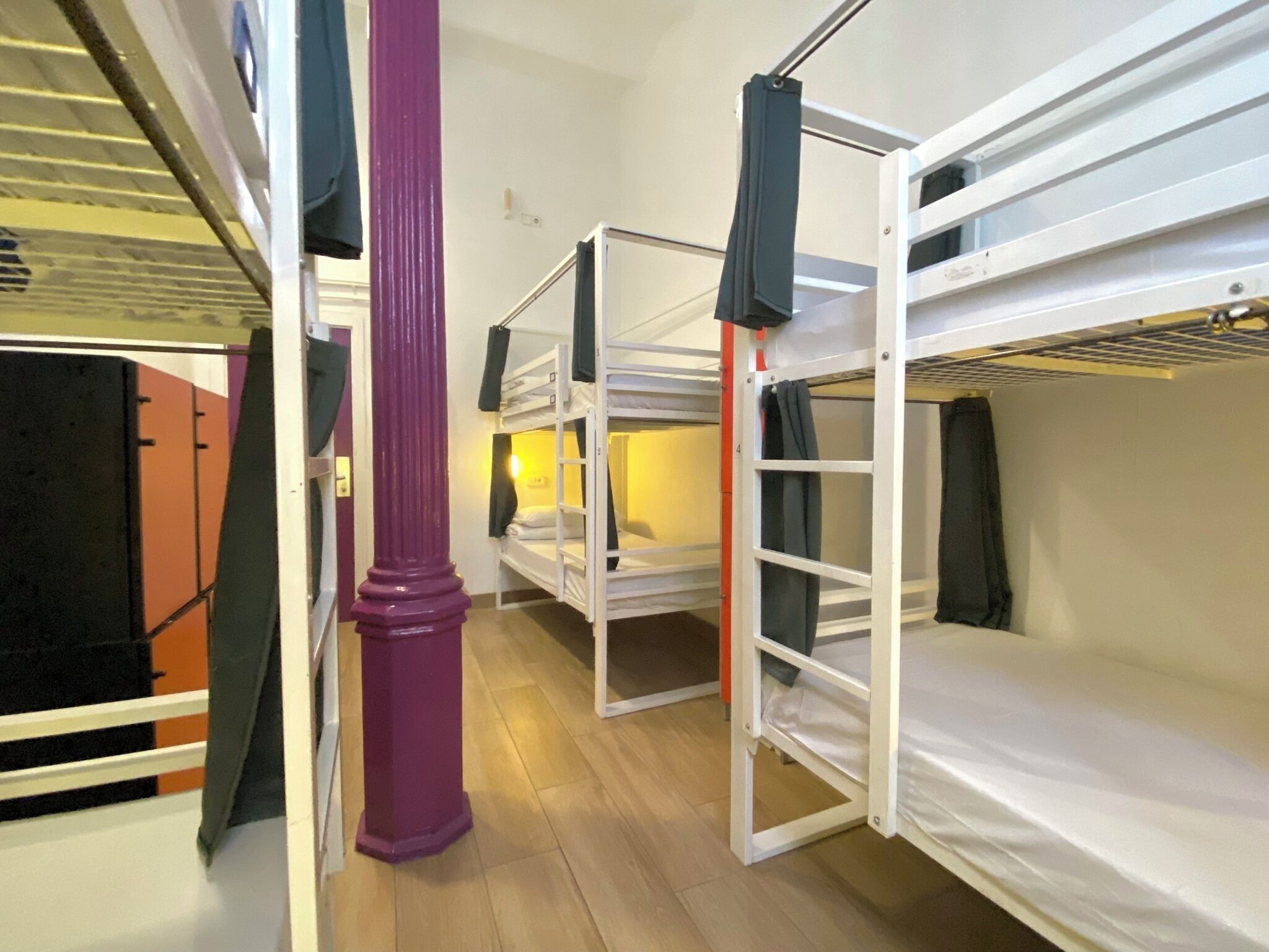 A dormitory room with bunk beds, a purple pillar, and a window with curtains.