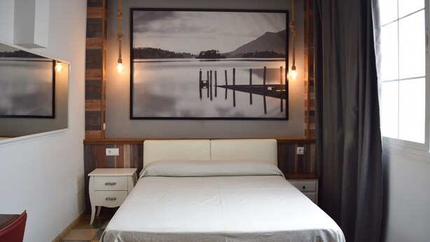 Une chambre à coucher comprenant un lit, des tables de chevet, une commode, un tableau accroché au mur et une fenêtre avec des rideaux.