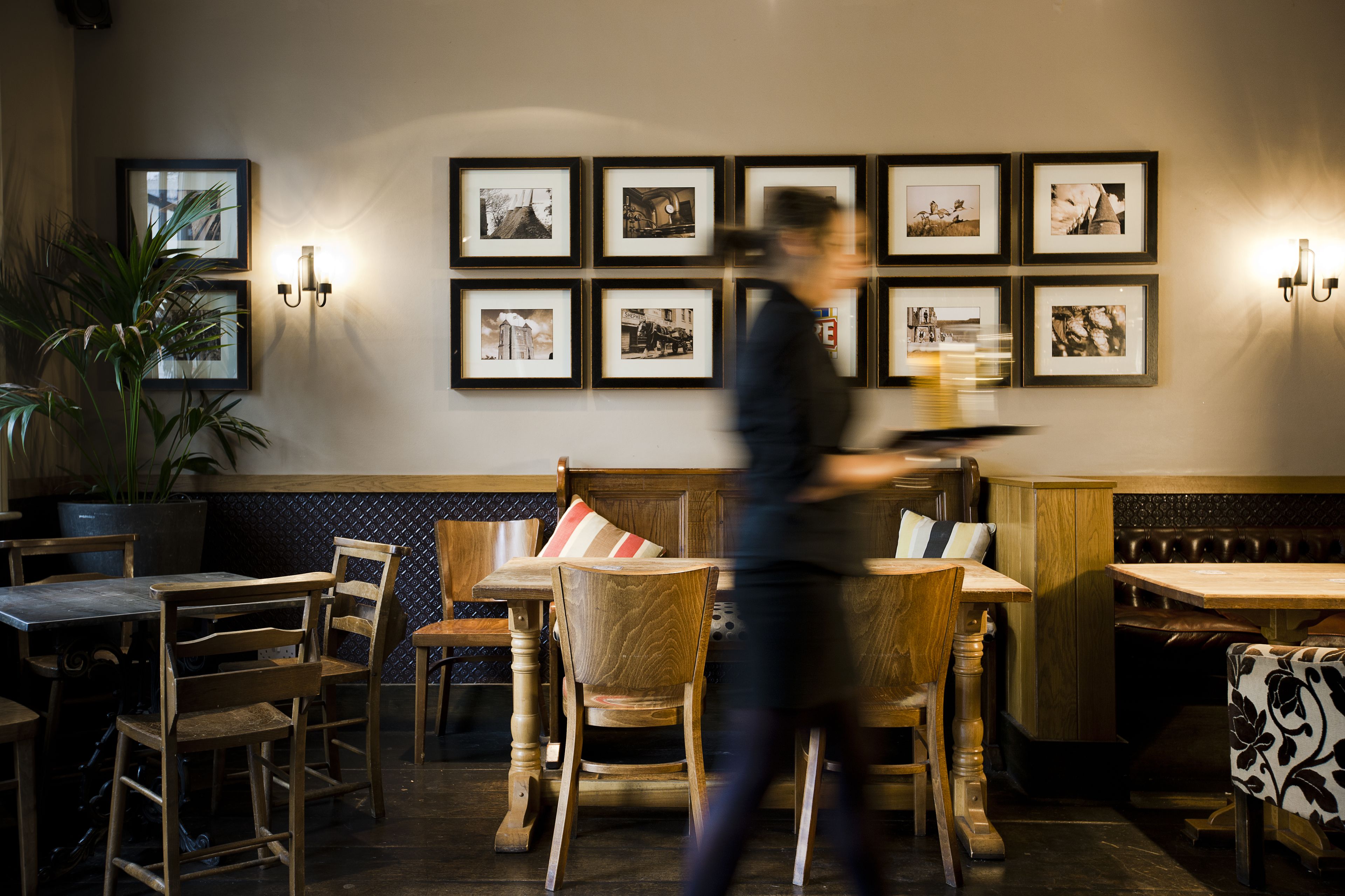 Un interior de restaurante con muebles de madera, una planta en maceta y cuadros en la pared.