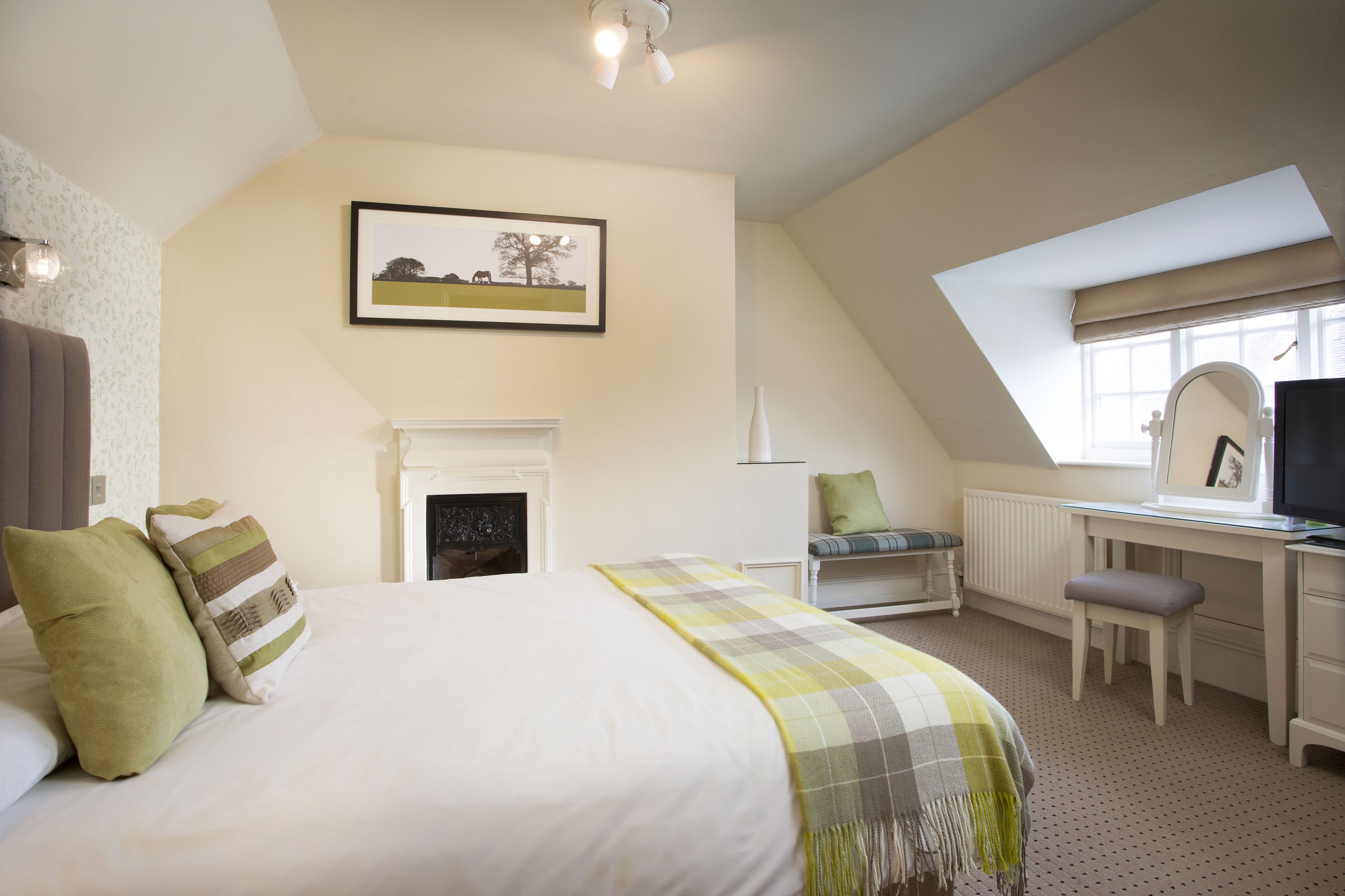 A bedroom with a bed, a desk, a chair, a fireplace, and a window.