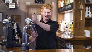 A barista at work, preparing a drink with a tap and a glass. - The George Hotel (Cranbrook)