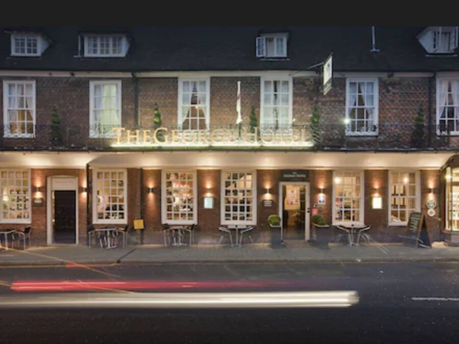 Il s’agit d’un bâtiment traditionnel en briques, sur lequel on peut lire l’inscription « The George Hotel ». Il est doté de nombreuses fenêtres, d’une terrasse et d’une façade bien éclairée.