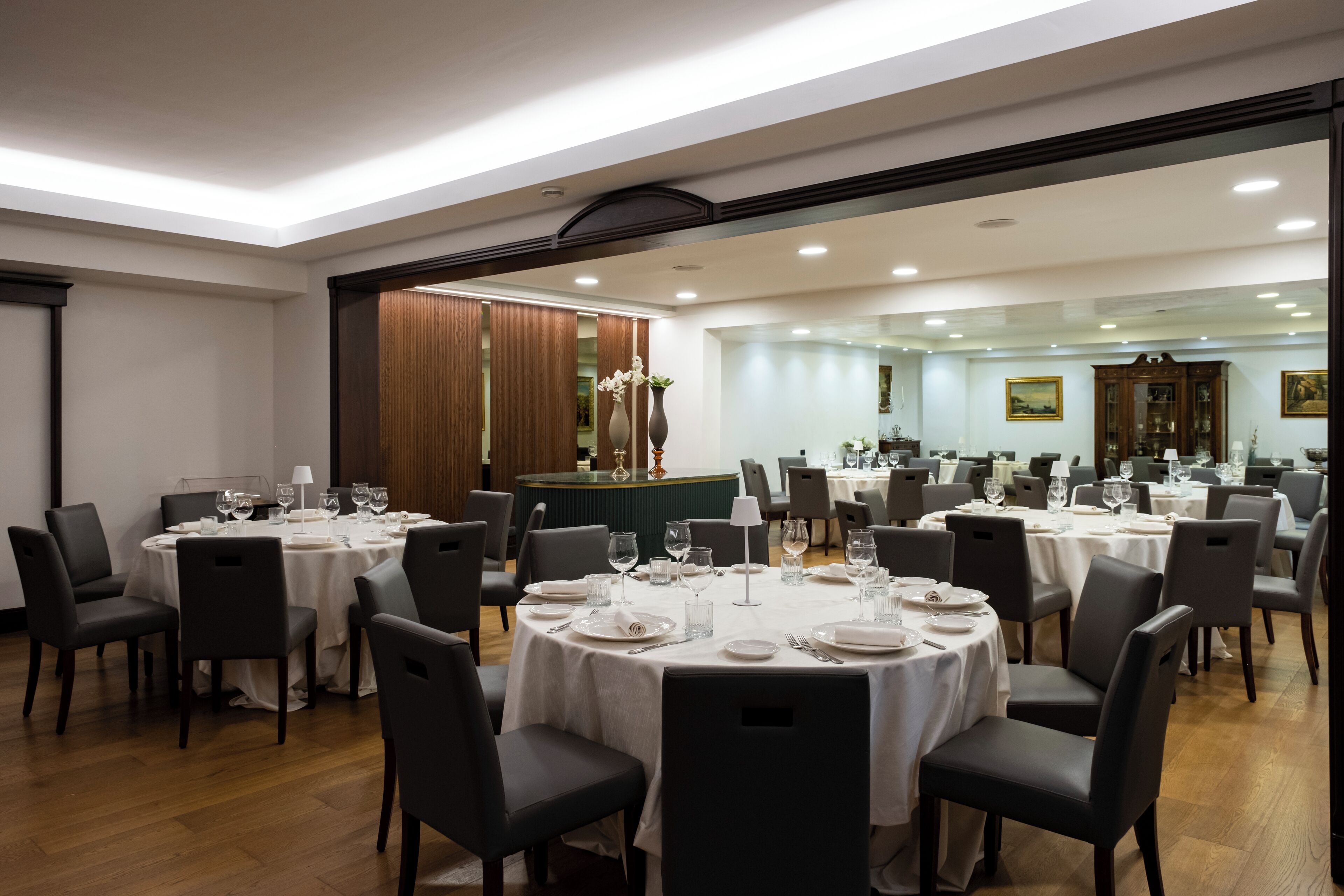 A restaurant with round tables set for dining, wooden flooring, and a large mirror reflecting the dining area.