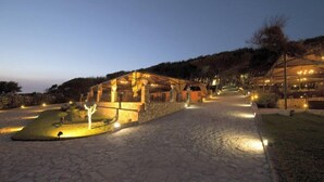 A stone pathway leading to a building with a glass facade, surrounded by trees and lit by warm lights. - Baia di Ulisse Wellness & SPA (Agrigento)