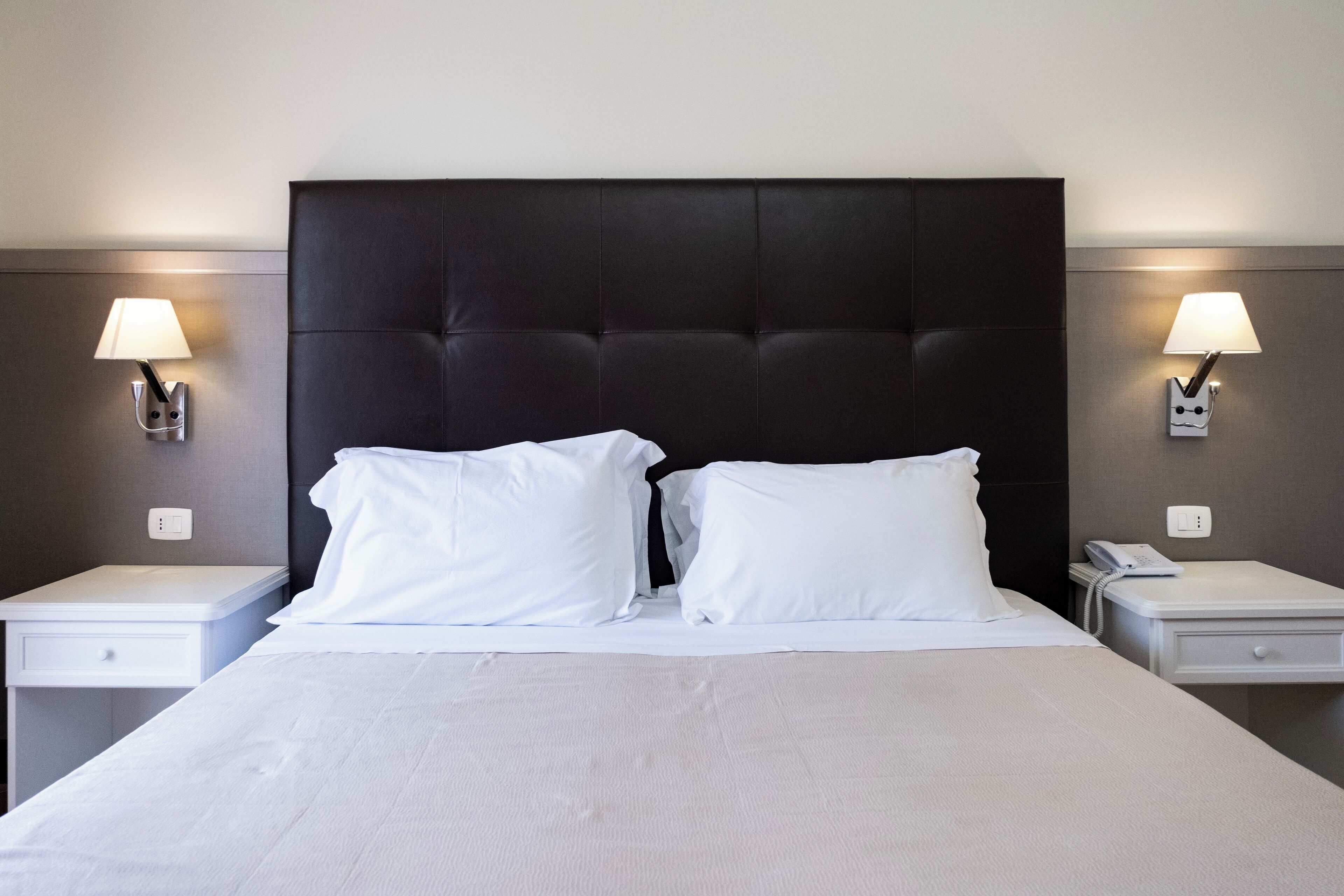 Une chambre d’hôtel avec un grand lit, deux tables de chevet et des lampes fixées au mur.
