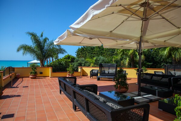 A terrace with outdoor furniture, a view of the sea, and potted plants.