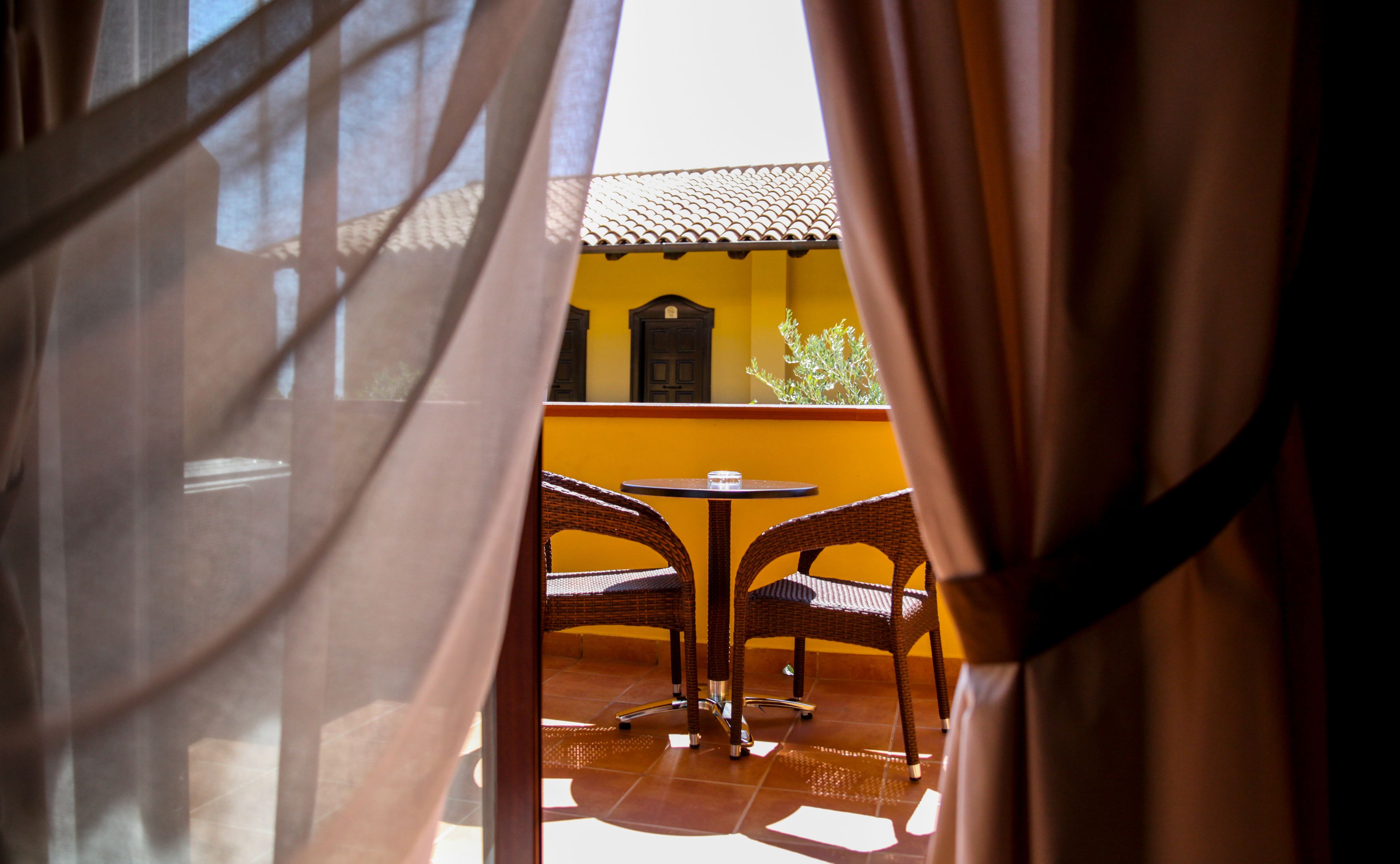 An outdoor patio with wicker chairs and a small round table, a yellow wall, and a tiled roof.