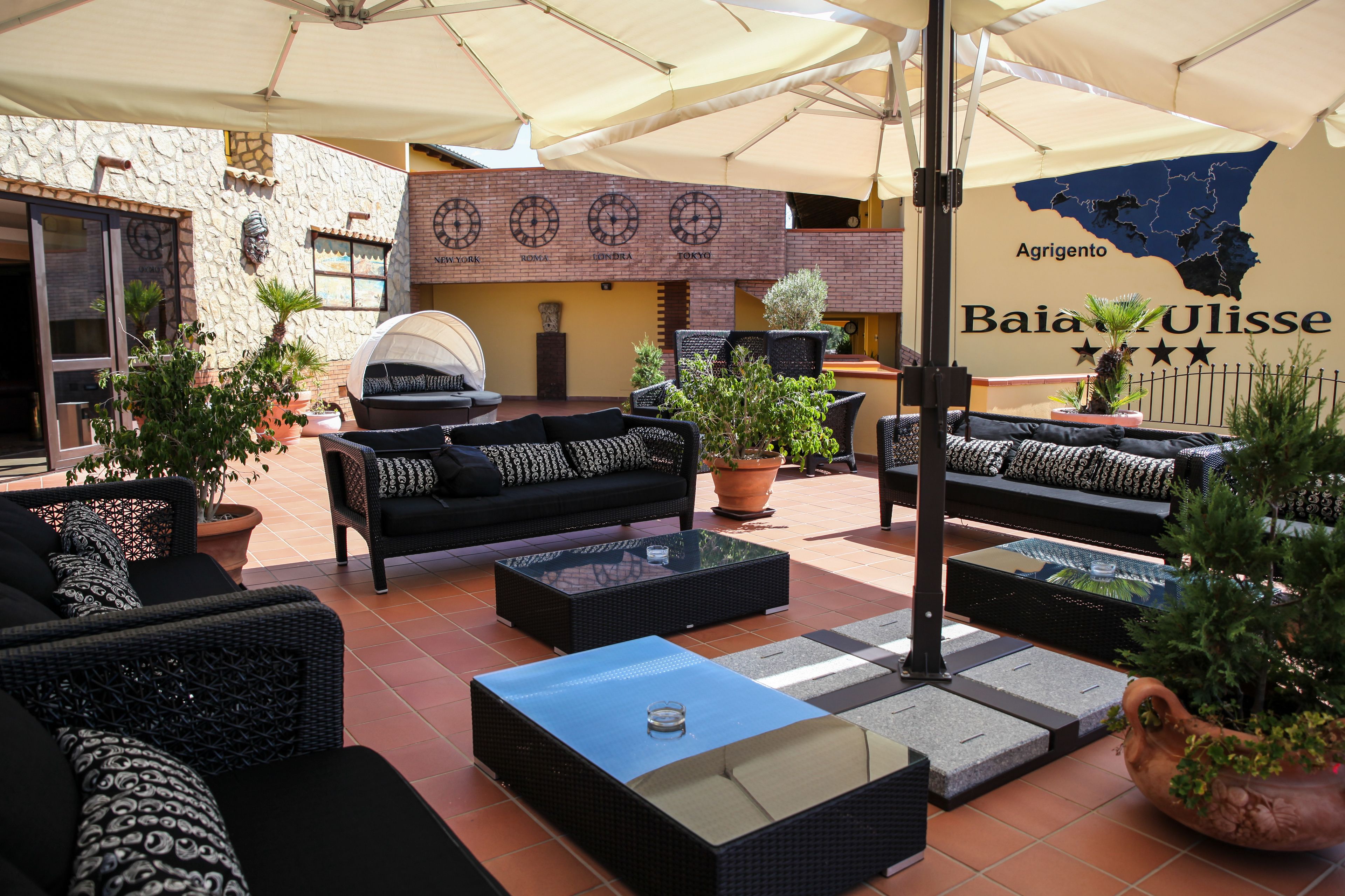 An outdoor seating area with wicker furniture, potted plants, and a map on the wall.