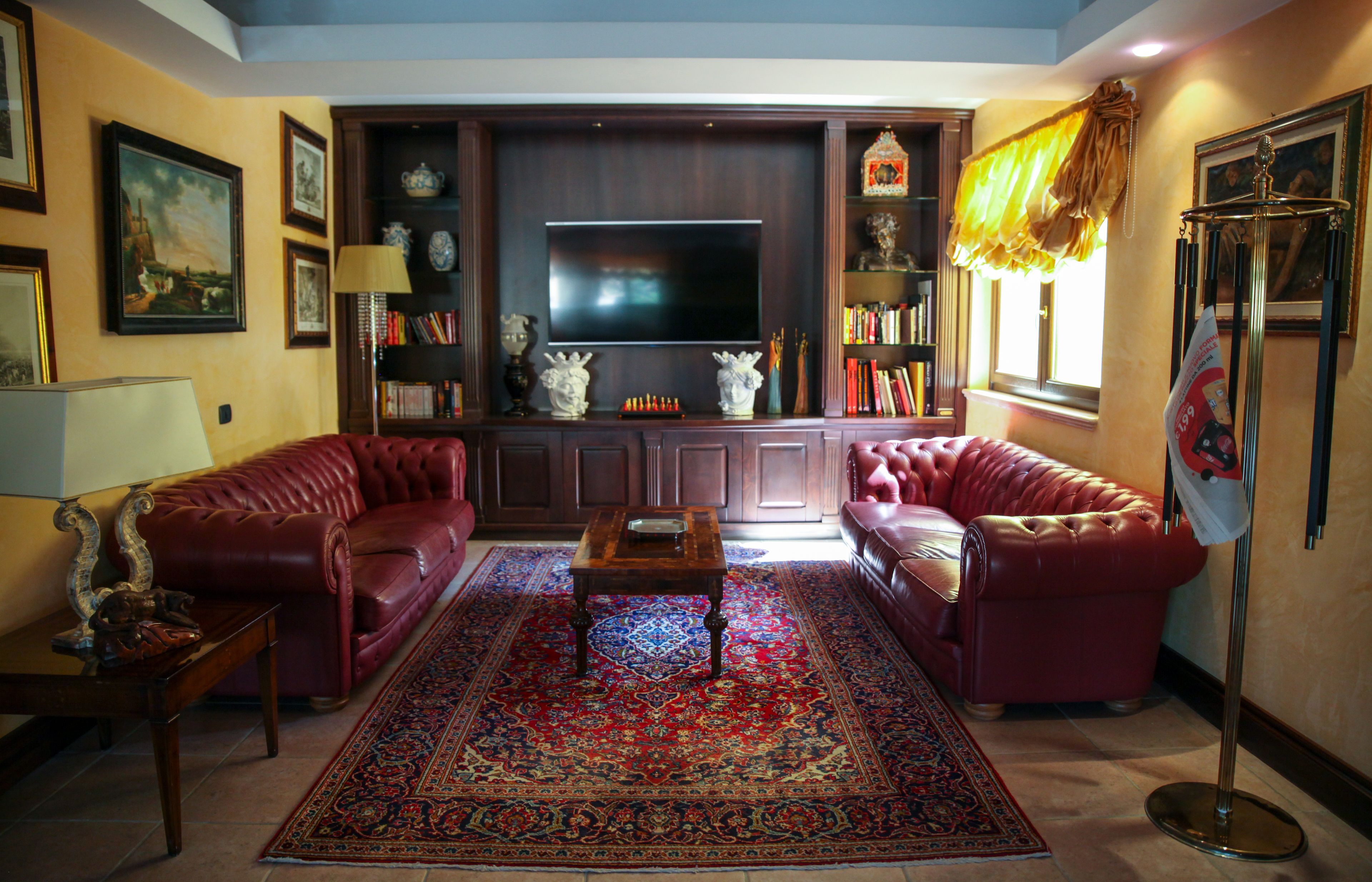 A living room with two red leather sofas, a wooden coffee table, a large flat-screen TV, and a decorative rug.