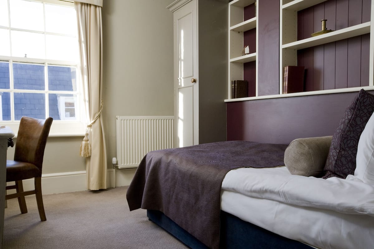 A bedroom with a bed, a chair, a window, and built-in shelving.