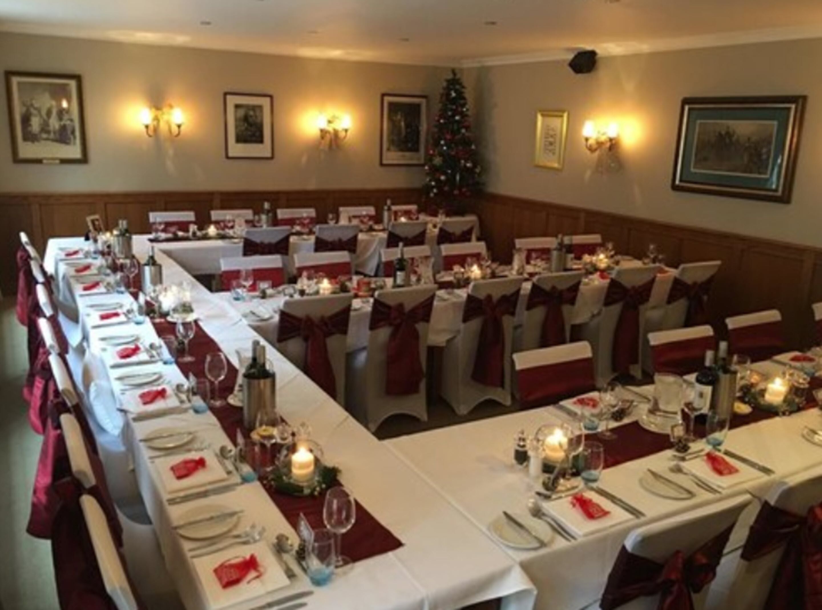 A banquet hall with long tables set for a formal event, decorated with candles and red sashes.