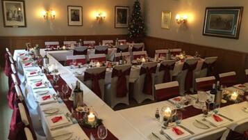 A banquet hall with long tables set for a formal event, decorated with candles and red sashes.