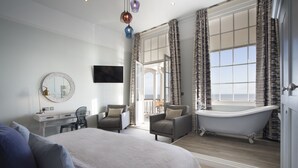 Une chambre spacieuse avec un grand lit, un coin salon avec des fauteuils, une coiffeuse avec un miroir et une baignoire sur pieds de style classique.