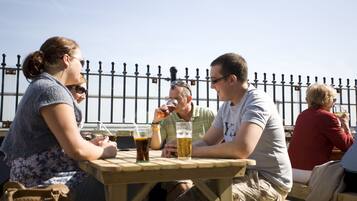 A group of people sitting at a wooden table outdoors, with drinks in front of them.