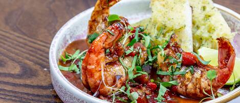 A bowl of seafood dish with bread on a wooden table.