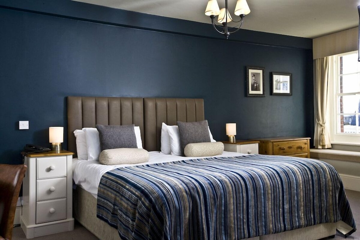 A bedroom with a large bed, bedside tables, a nightstand, a chair, and a window with curtains.