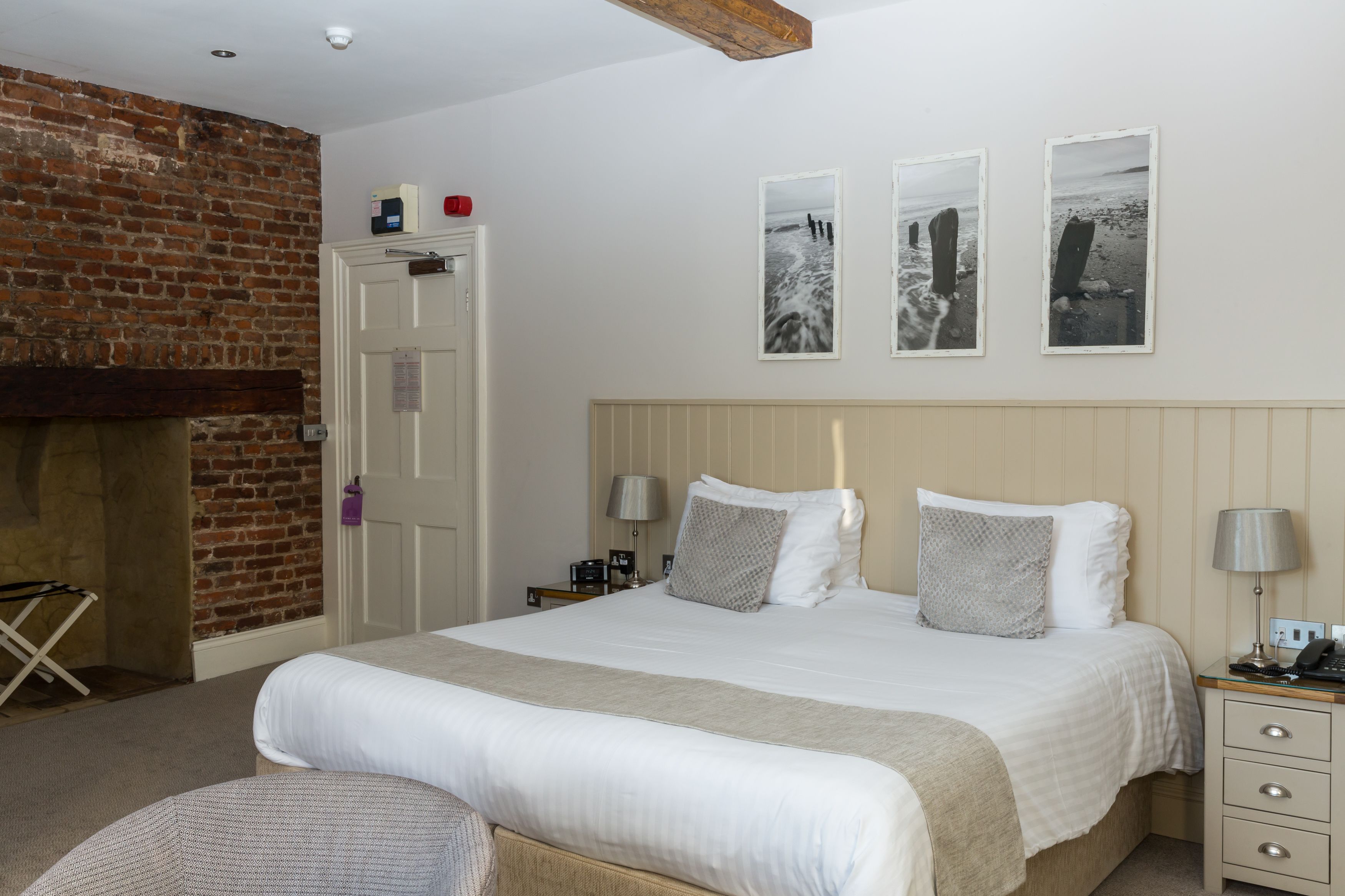 A bedroom with a large bed, a wooden headboard, a nightstand with a lamp, and a brick wall.