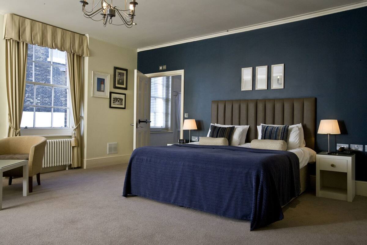 A bedroom with a bed, bedside tables, a chair, a radiator, and a window with curtains.