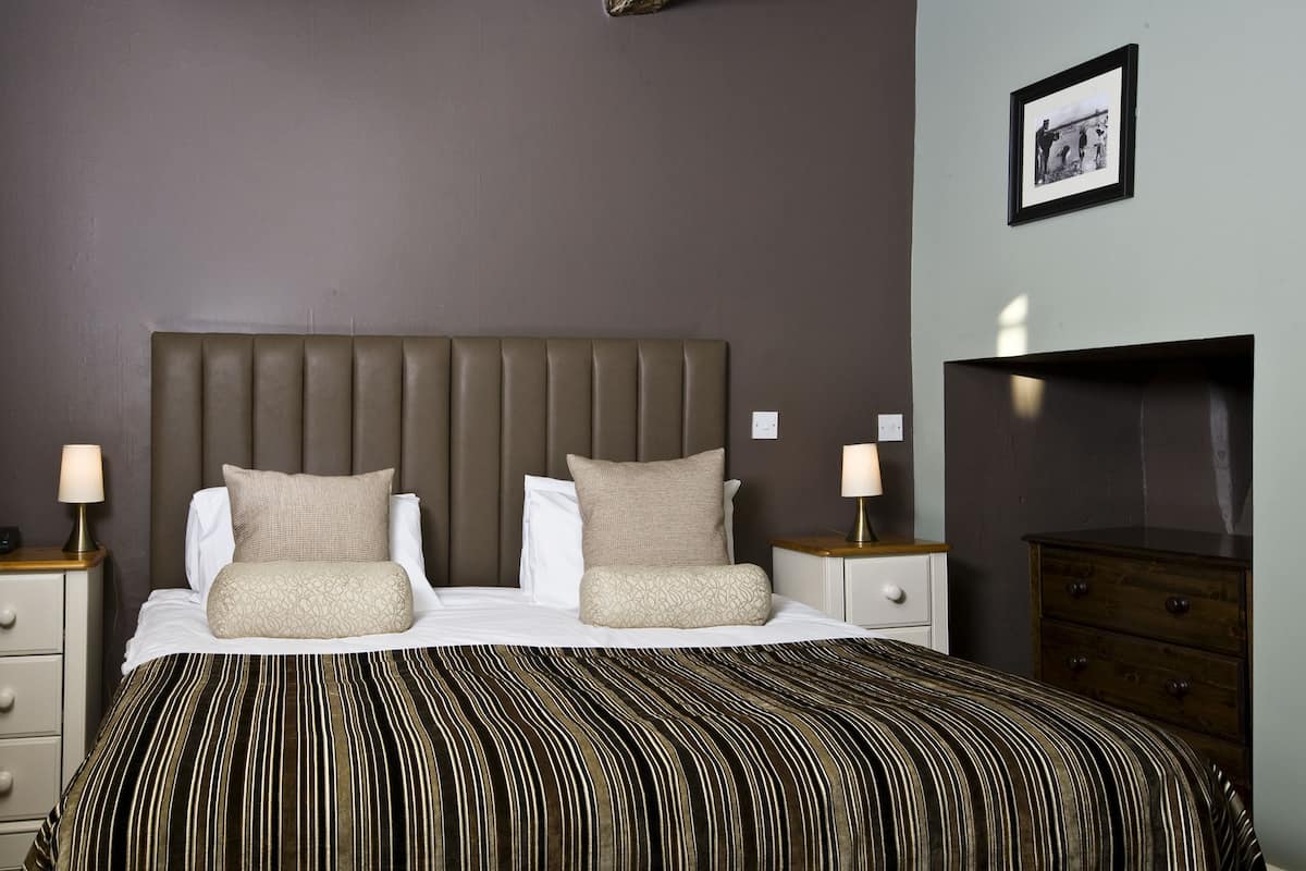 A neatly arranged bedroom with a large bed, two bedside tables, a dresser, and a framed picture on the wall.