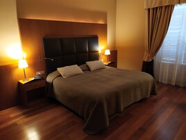 A neatly made bed with a headboard, two bedside lamps, and a window with curtains.