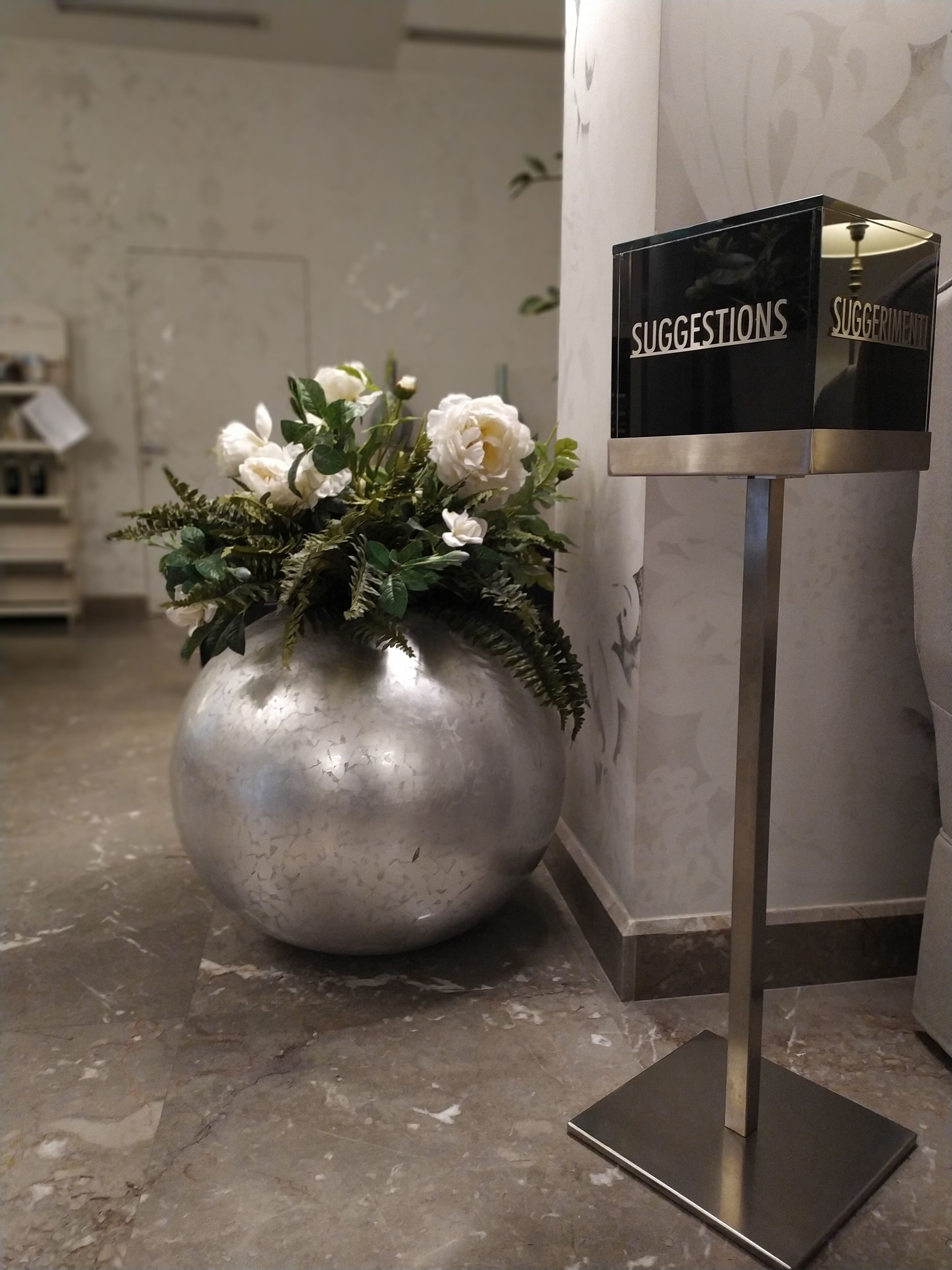 A marble reception desk with a suggestions box and a large vase of white flowers.