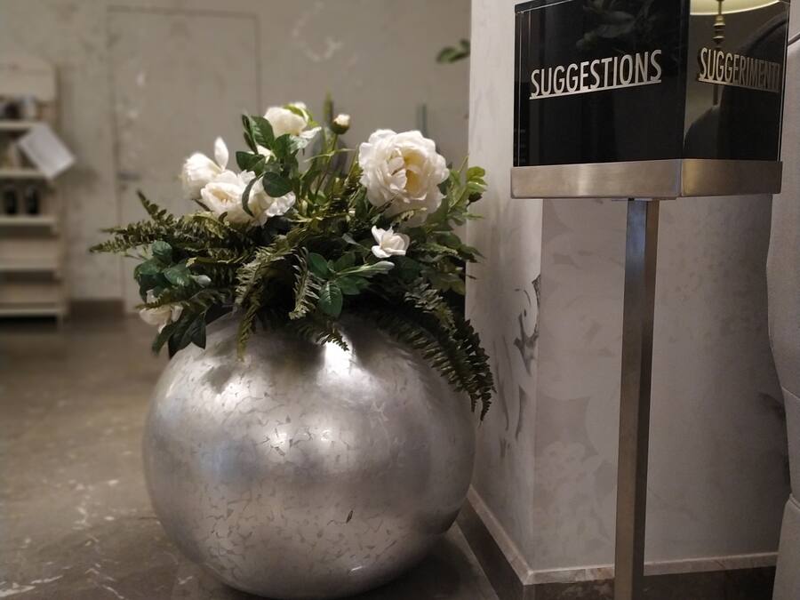A marble reception desk with a suggestions box and a large vase of white flowers.