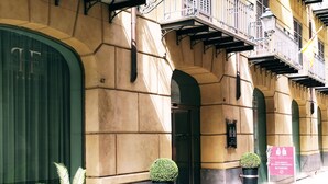 Une façade d’immeuble avec une grande porte verte, un balcon doté de rampes en métal et une enseigne indiquant qu’il s’agit d’un hôtel.