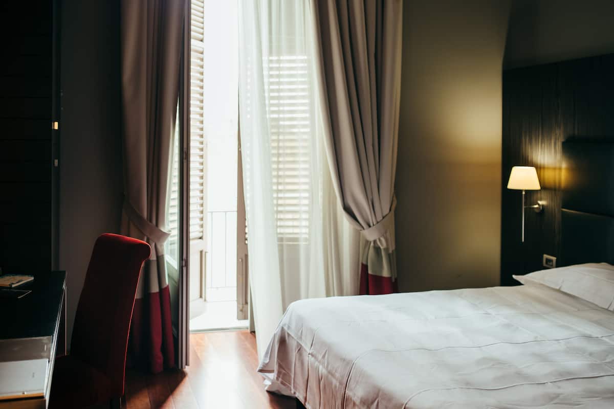 A hotel room with a bed, a desk, and a chair. There is a window with curtains.