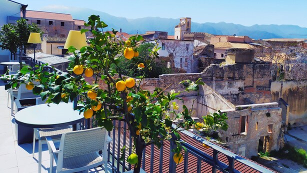 Une terrasse avec des sièges en plein air, un arbre aux citrons et, en arrière-plan, des bâtiments historiques.