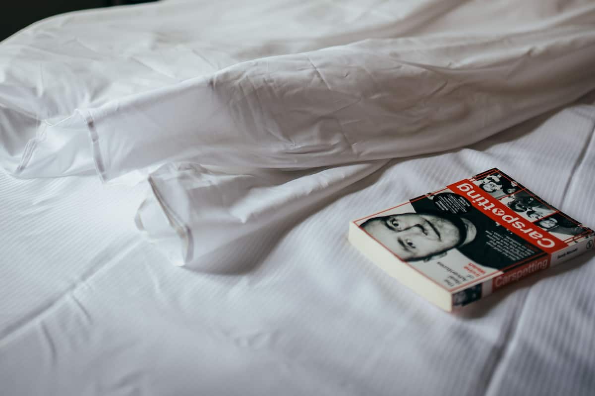 A neatly made bed with white linens and a book titled "Carpeting" on it.