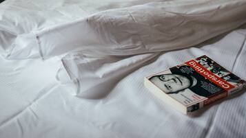A neatly made bed with white linens and a book titled "Carpeting" on it.