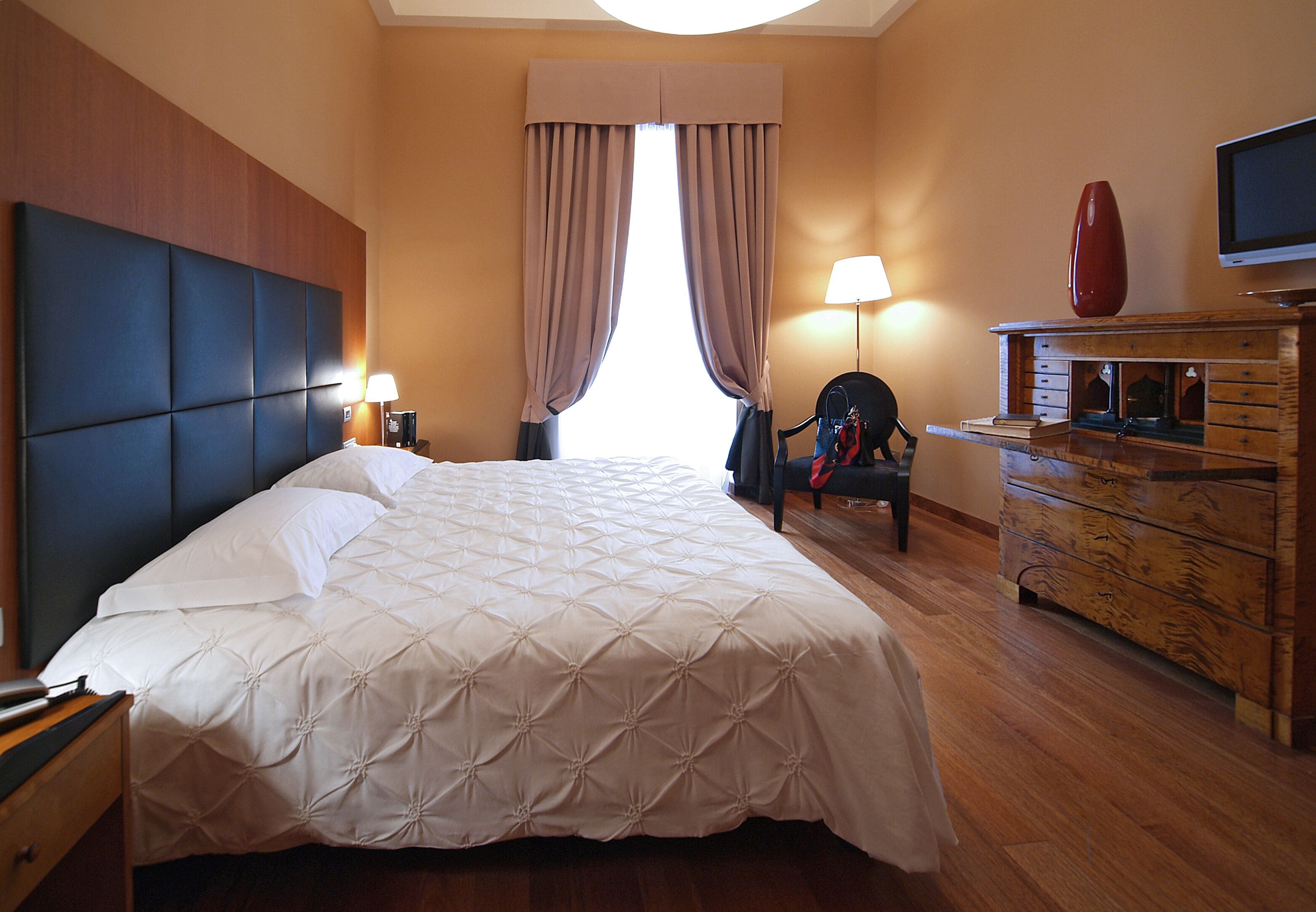 Una camera d'albergo con un letto grande, una cassettiera in legno, una televisione e una sedia.