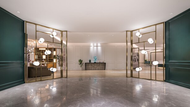 Um hall espaçoso com chão de mármore polido, um balcão de recepção central e vista para um quarto bem iluminado com uma janela grande.