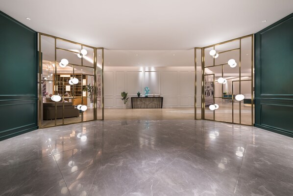 A spacious lobby with a polished marble floor, a central reception desk, and a view into a well-lit room with a large window.