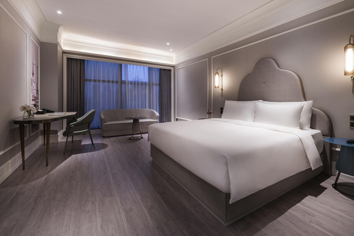 A hotel room with a large bed, a desk, a chair, and a sofa.