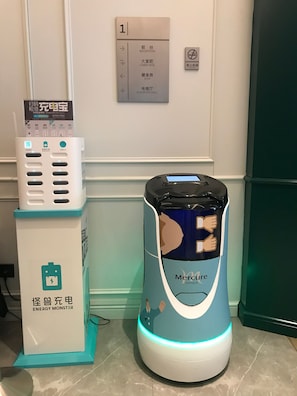 A hotel reception area with a self-service kiosk, a charging station, and a robot vacuum cleaner.