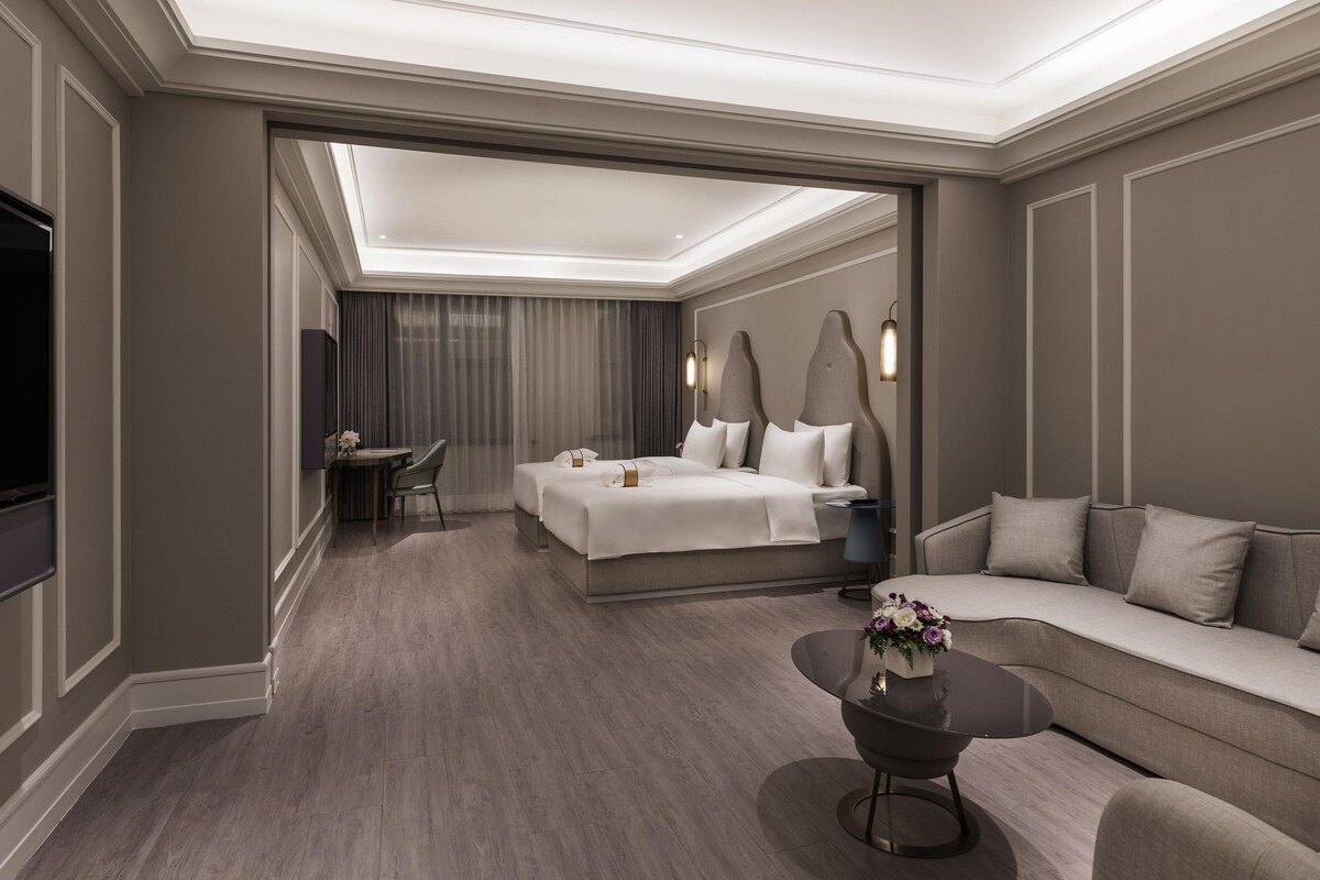 A modern hotel room with a large bed, a sofa, a coffee table, and a TV.