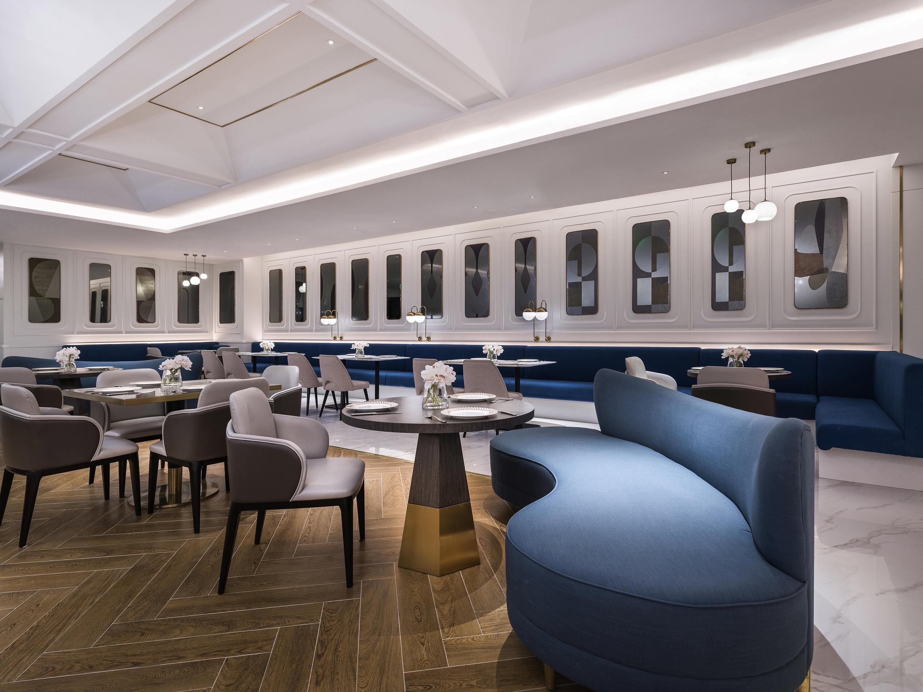 A modern dining area with high ceilings, recessed lighting, and a row of booths and tables.