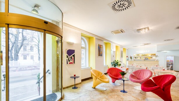 A hotel lobby with a glass entrance, modern chairs, a bar area, and artwork on the walls. - Hotel Europa (Brno)