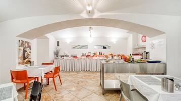 A dining area with a buffet setup, tables, chairs, and a tiled floor.