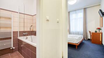 A hotel room with a shower, a bed, a desk, and a window with curtains.