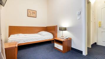 A hotel room with a wooden bed, a nightstand with a lamp, a small drawer, and a world map on the wall.